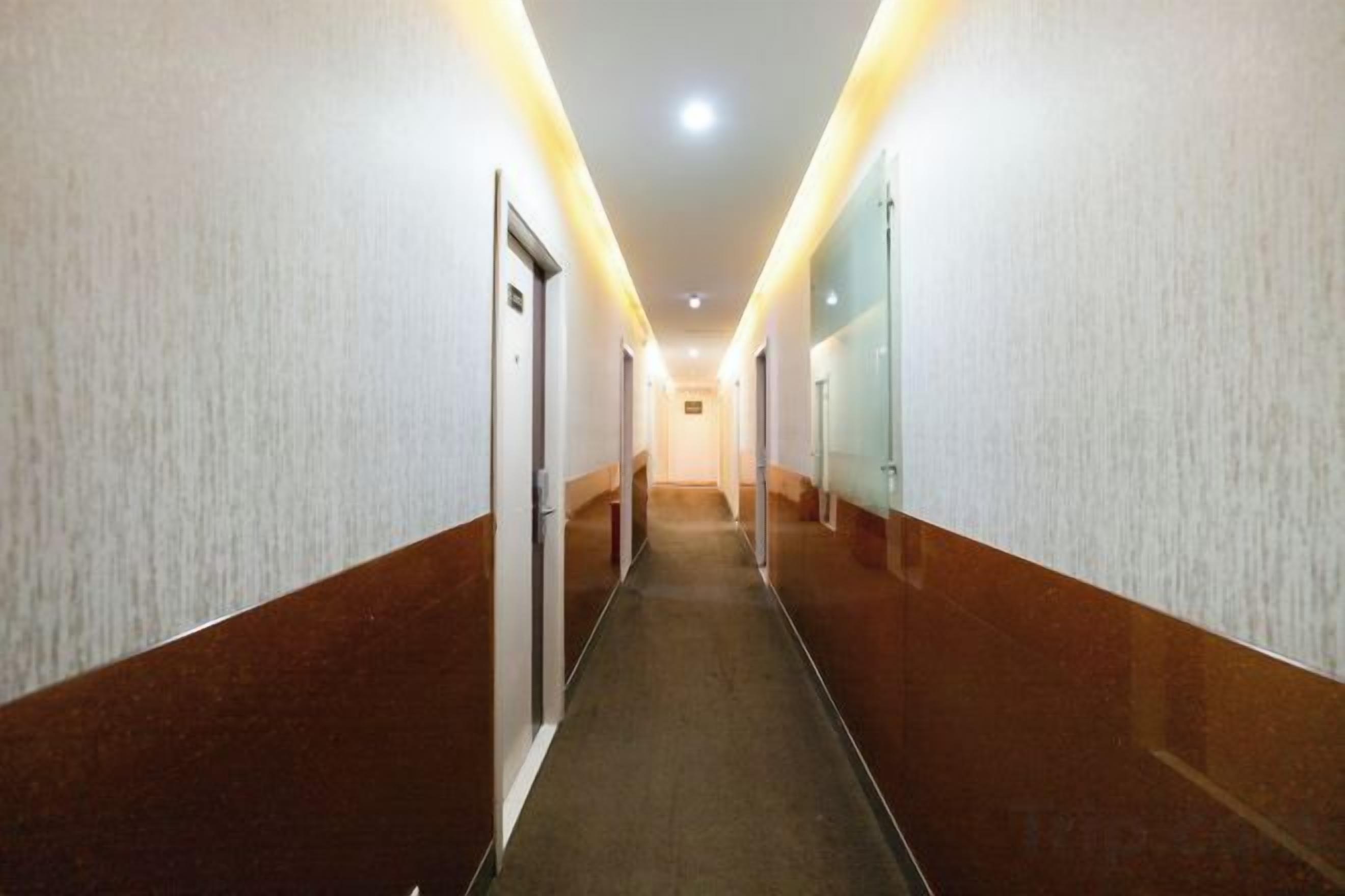 A long, narrow hotel corridor with doors on both sides, recessed lighting, and a carpeted floor.
