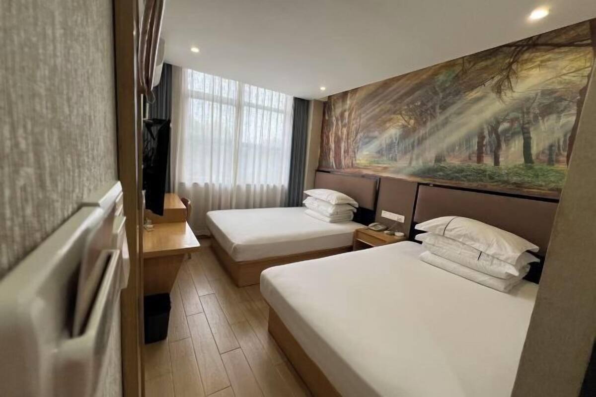 Ein Hotelzimmer mit zwei Betten, einem Bild an der Wand, einem Schreibtisch und einem Fenster mit Vorhängen.