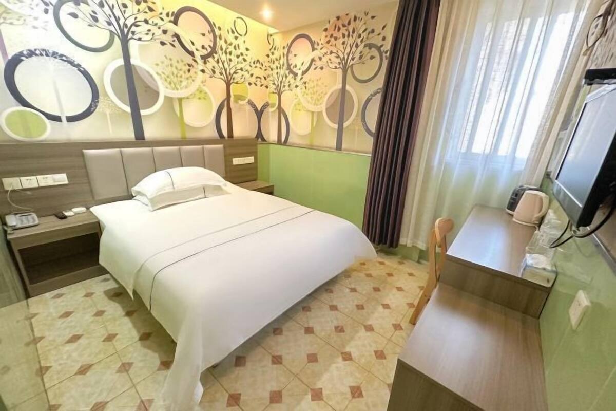 Ein Hotelzimmer mit einem Bett, einem Nachttisch mit Telefon, einem Sessel, einem kleinen Schreibtisch und einer Wand mit Baumdekor.