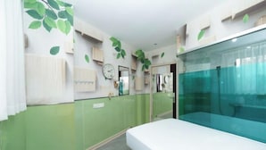 Una habitación con cama, espejo, reloj y pared verde con diseños de hojas.