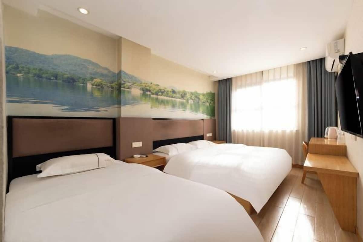 Ein Hotelzimmer mit zwei Betten, einem Schreibtisch, einem Fernseher und einem Gemälde von einem See.