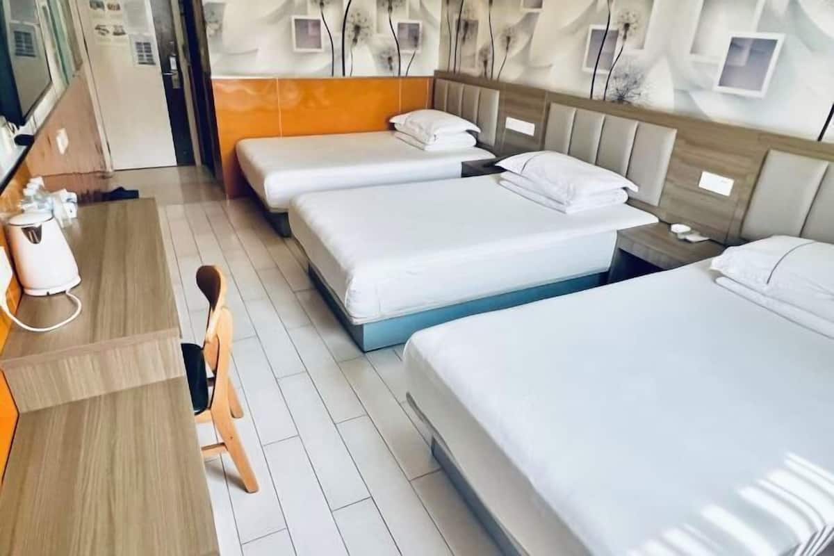 Ein Hotelzimmer mit drei Betten, einem Schreibtisch und einem Stuhl.