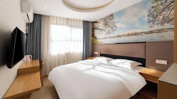 Habitación de hotel con cama, televisor de pantalla plana, un cuadro en la pared y una ventana con cortinas.