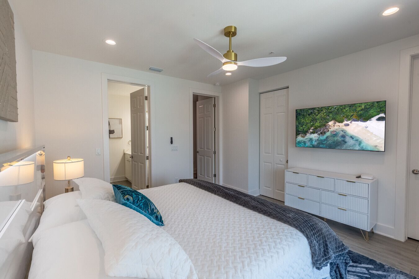 Un dormitorio con cama, lámparas de noche, ventilador de techo, televisor y vista al mar.