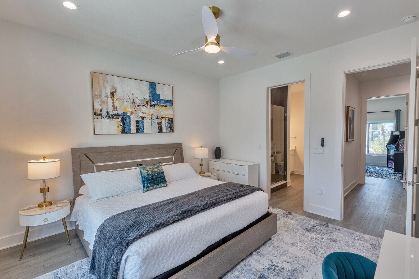 A modern bedroom with a large bed, bedside tables, a ceiling fan, and a painting on the wall.