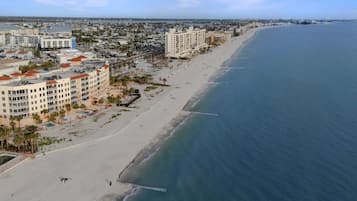 Vista aérea de una ciudad costera con una extensa playa de arena, varios edificios de varios pisos y un océano azul cristalino.