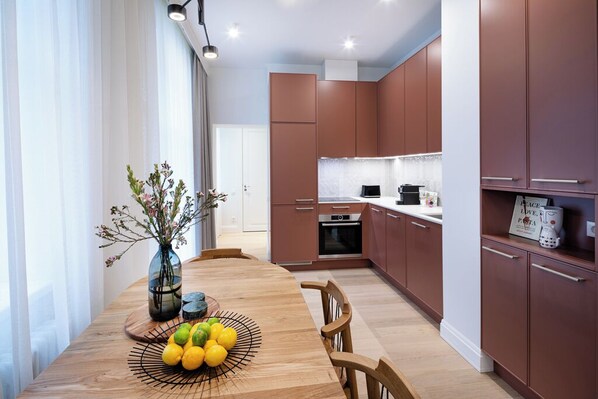 Une cuisine moderne avec des meubles en bois, une table à manger agrémentée d’un centre de table composé de fruits, et une vue sur le salon attenant.