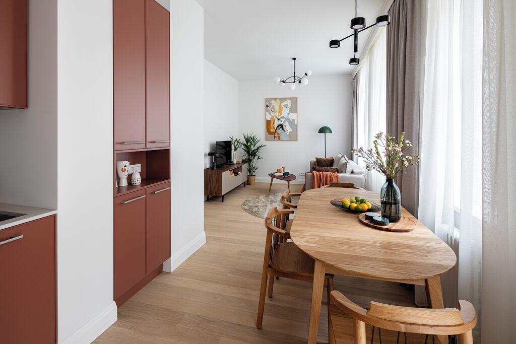 Una cocina moderna con armarios de madera, una mesa de comedor con sillas y vistas a una sala de estar con sofá y plantas.