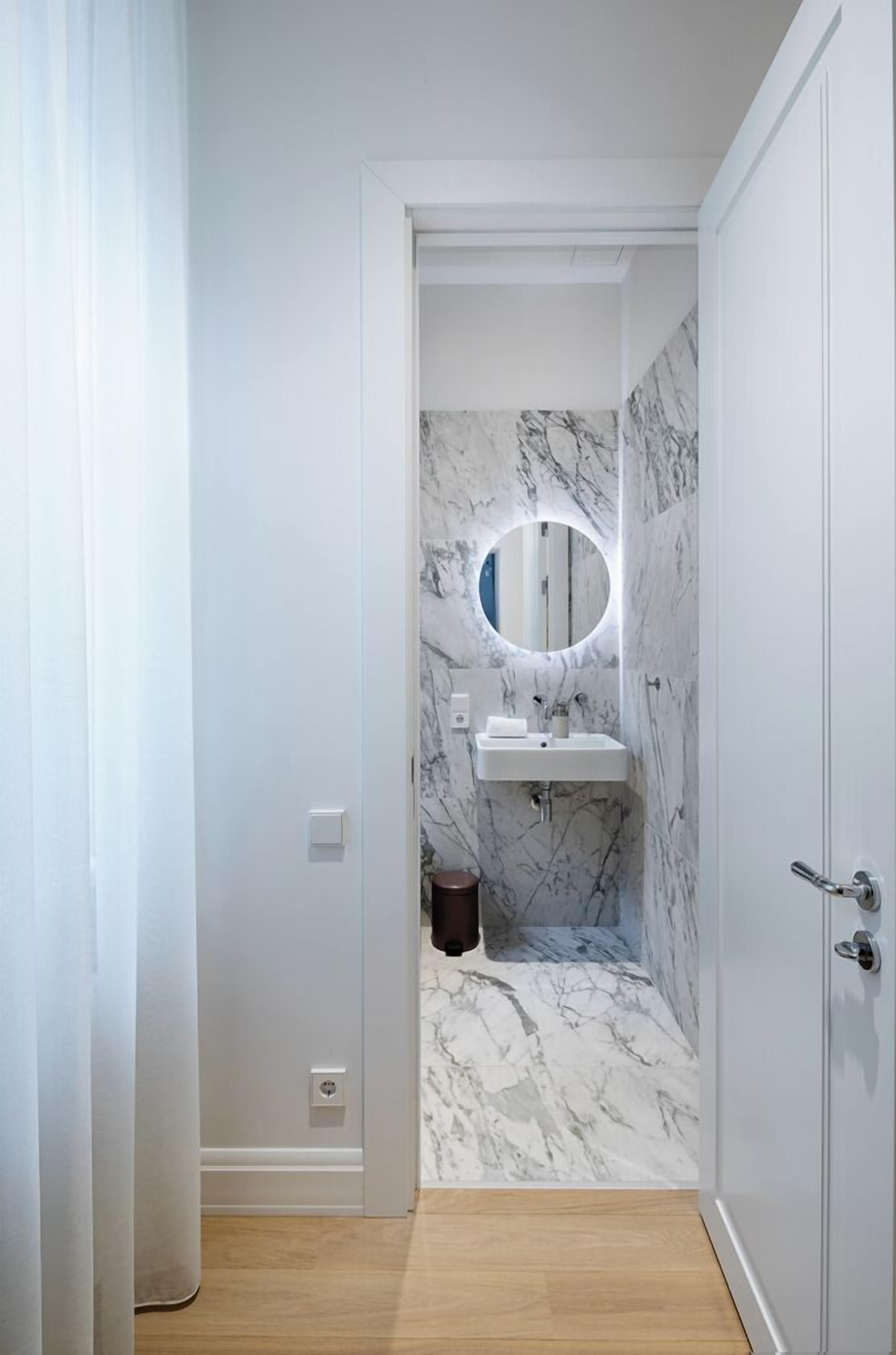 Un baño moderno con pared de mármol, espejo redondo y lavamanos blanco.