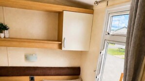 A compact RV interior with two beds, a small kitchenette, and a window with curtains. - Caravan Meg Sleeps 6 With Free Parking (Rhyl)