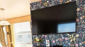 A modern living space with a flat-screen TV mounted above a fireplace with a floral backsplash. - Caravan Meg Sleeps 6 With Free Parking (Rhyl)