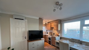 A compact kitchen with a TV, cabinets, a dining table with chairs, and a window with blinds.
