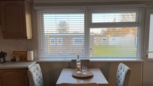 A dining area with a table and two chairs, a window with blinds, and a view of a yard.