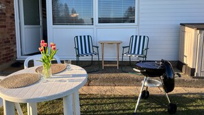 A patio with two chairs, a table with a vase of flowers, and a grill.