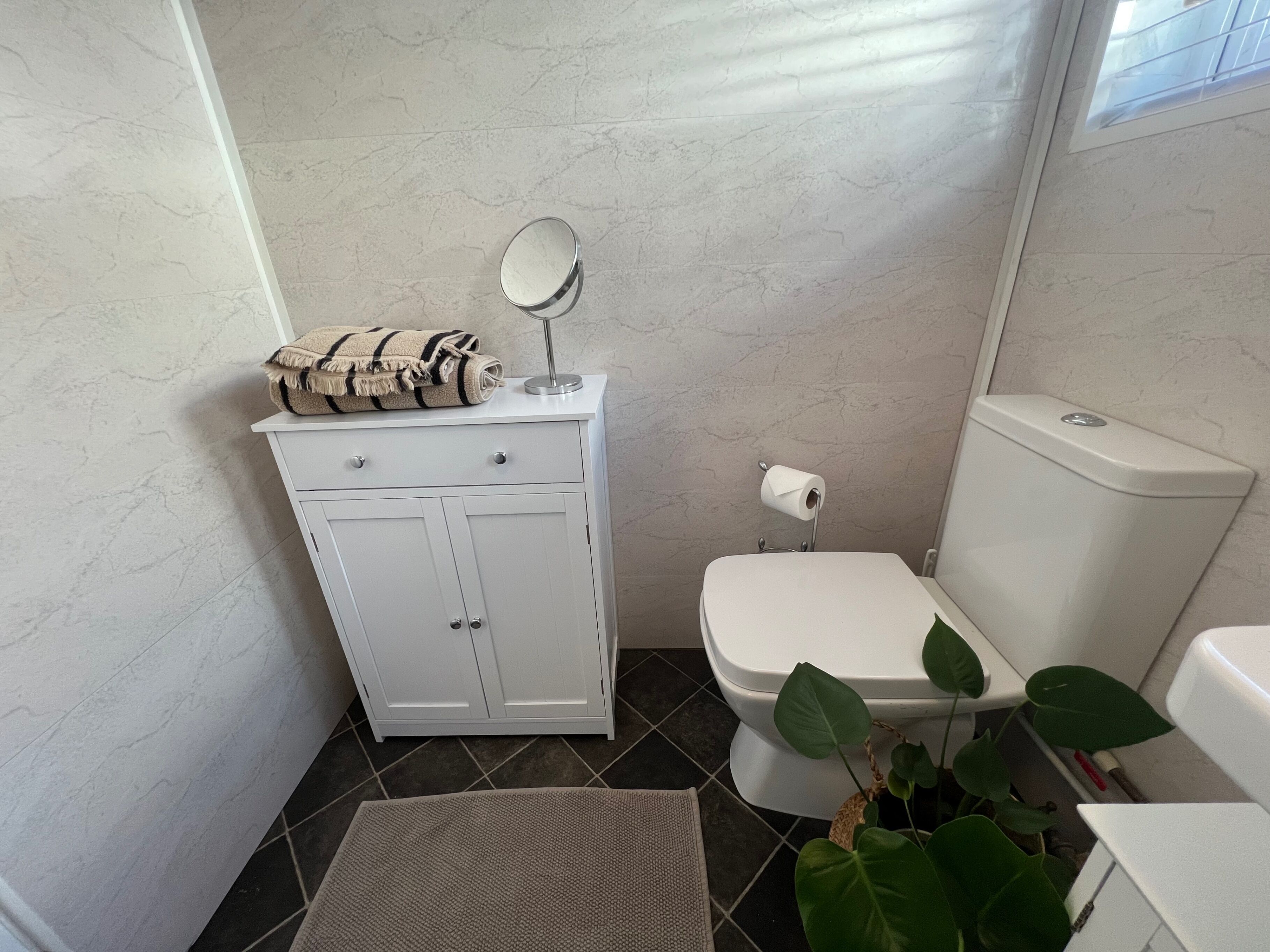 Ein Badezimmer mit weißem Schrank, Toilette und Pflanze.