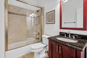 A bathroom with a glass-enclosed shower, a white toilet, a sink with a dark countertop, and a mirror with a red frame.