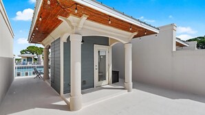 Egy fedett, szabadtéri terület, melynek mennyezete és oszlopai fából vannak, van rajta egy ajtó, és a háttérben egy medence látható.