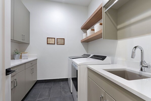 Una cocina moderna con armarios blancos, lavavajillas integrado, un lavamanos de acero inoxidable y estantes de madera sobre la encimera.