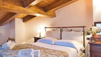 Un dormitorio con techo de madera, una cama con ropa de cama blanca, una mesita de noche con una lámpara y un aparador de madera.