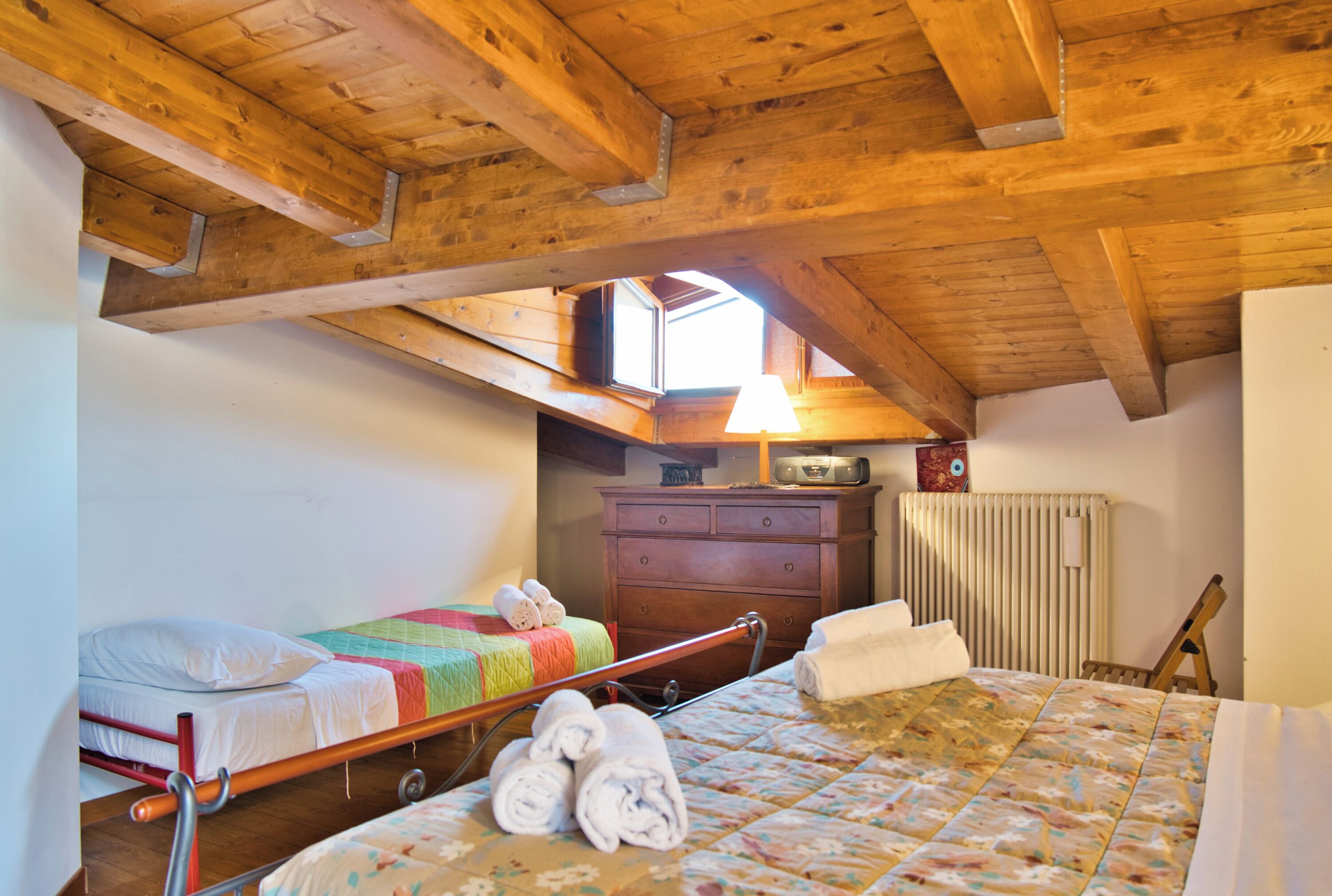 Een slaapkamer met een houten plafond, een bed met een bloemenbedekking, een nachtkastje, een dressoir en een raam met uitzicht.