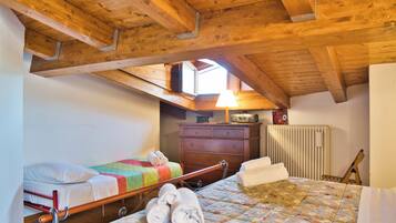 Een slaapkamer met een houten plafond, een bed met een bloemenbedekking, een nachtkastje, een dressoir en een raam met uitzicht.