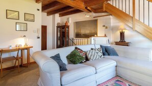 A cozy living room with a white sofa, wooden beams, a staircase, and a large painting on the wall. - La Dimora del Borgo - Two Bedroom House, Sleeps 6 (Lierna)