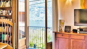 Una habitación con una estantería de madera, un televisor y vistas a un lago a través de una puerta de balcón.