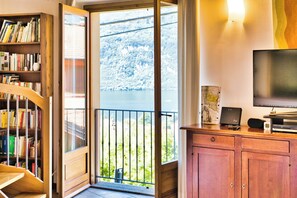 A room with a wooden bookshelf, a television, and a view of a lake through a balcony door.