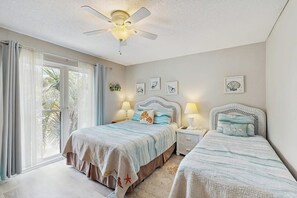 Une chambre avec deux lits, un ventilateur de plafond et une grande fenêtre avec des rideaux.