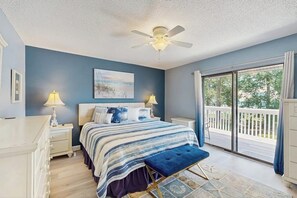 A bedroom with a bed, nightstands, a ceiling fan, a window with a view, and a balcony.