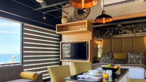 Une chambre d’hôtel moderne dotée d’une grande télévision, de sièges confortables, d’un coin repas et offrant une vue sur la mer.