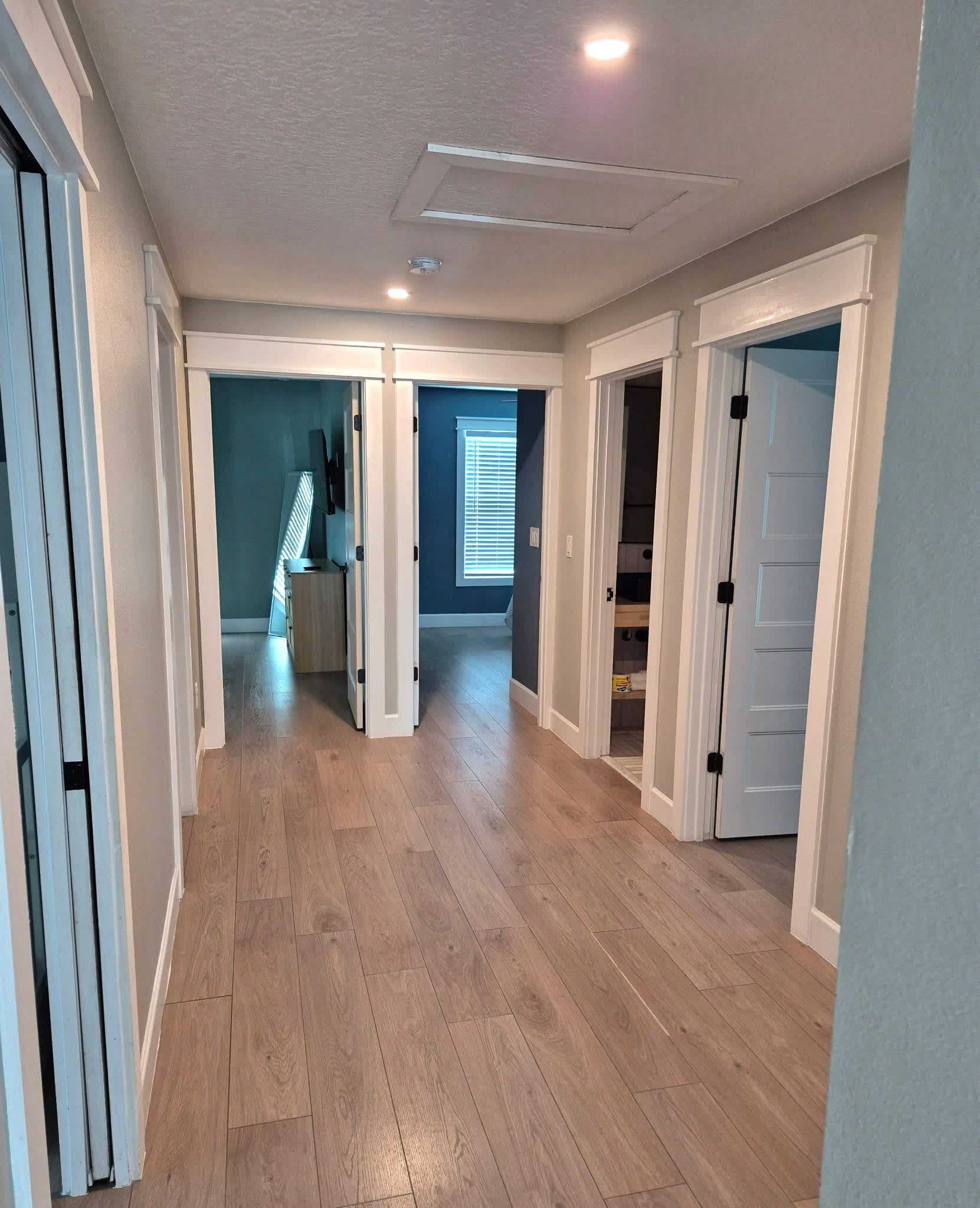 A spacious hallway with wooden flooring, white walls, and multiple doors leading to different rooms.