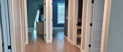 Un pasillo amplio con suelo de madera, paredes blancas y varias puertas que dan a diferentes habitaciones.