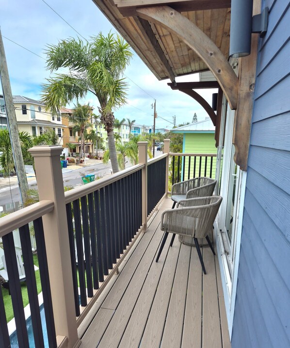 A wooden deck with a railing, two wicker chairs, and a view of a street with houses and palm trees.