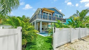 Ein zweistöckiges Haus mit Balkon, Swimmingpool und üppiger tropischer Vegetation.