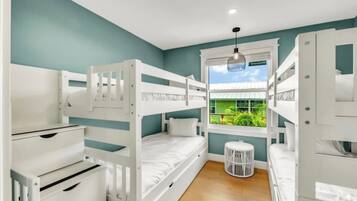 A room with bunk beds, a window with a view of greenery, and a white circular stool.