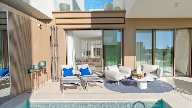 Ein moderner Poolbereich im Freien mit Liegestühlen, einem Esstisch und Blick ins Wohnzimmer.