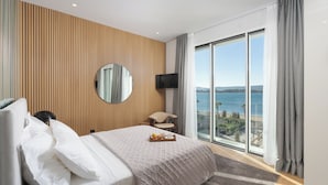Ein Hotelzimmer mit einem großen Bett, einem Fernseher, einem Sessel und Blick auf das Meer.