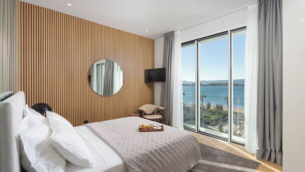 Une chambre d’hôtel avec un grand lit, une télévision, un fauteuil et une vue sur la mer.