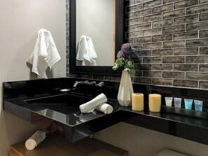 A modern bathroom with a black sink, two white towels, a vase with flowers, and candles.