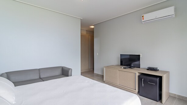 A hotel room with a bed, a sofa, a TV, a mini-fridge, and an air conditioning unit. - Mansão Carneiros By Carpediem (Tamandaré)