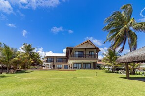 A two-story building with a balcony, surrounded by a well-maintained lawn and palm trees. - Mansão Carneiros By Carpediem (Tamandaré)