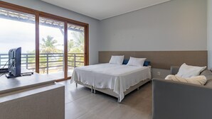 A hotel room with a bed, a desk with a computer, a chair, and a view of palm trees through large windows. - Mansão Carneiros By Carpediem (Tamandaré)