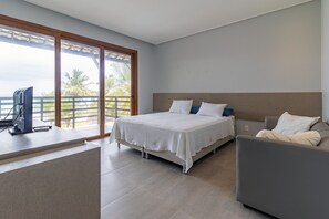 A hotel room with a bed, a desk with a computer, a chair, and a view of palm trees through large windows. - Mansão Carneiros By Carpediem (Tamandaré)