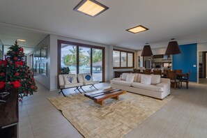 A spacious living room with a large window, a sofa set, a coffee table, and a Christmas tree. - Mansão Carneiros By Carpediem (Tamandaré)