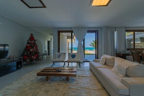 A modern living room with a large window overlooking a beach, a Christmas tree, and a cozy seating area. - Mansão Carneiros By Carpediem (Tamandaré)