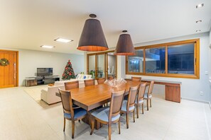 A modern dining area with a wooden table and chairs, a Christmas tree, and a large window. - Mansão Carneiros By Carpediem (Tamandaré)