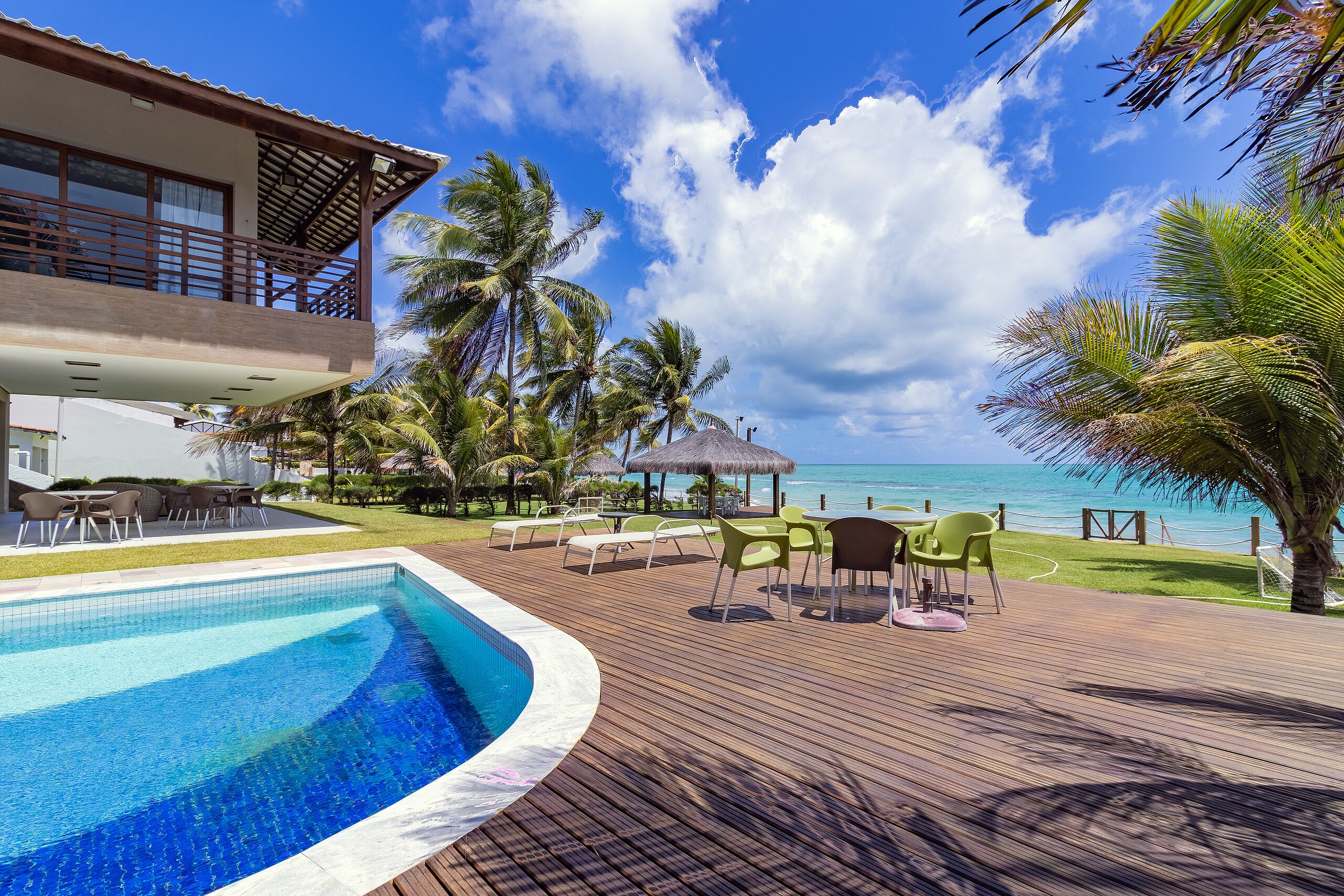 A poolside area with a clear view of the ocean, lounge chairs, and a building with a balcony.