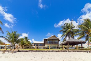 A beachfront property with a two-story building, a thatched-roof structure, and palm trees. - Mansão Carneiros By Carpediem (Tamandaré)