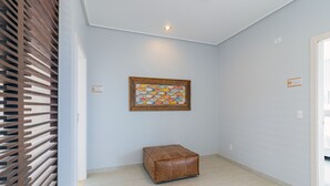 A hallway with a wooden slatted wall, a framed fish artwork, a brown leather ottoman, and a door labeled 'Suite Toquinho'. - Mansão Carneiros By Carpediem (Tamandaré)
